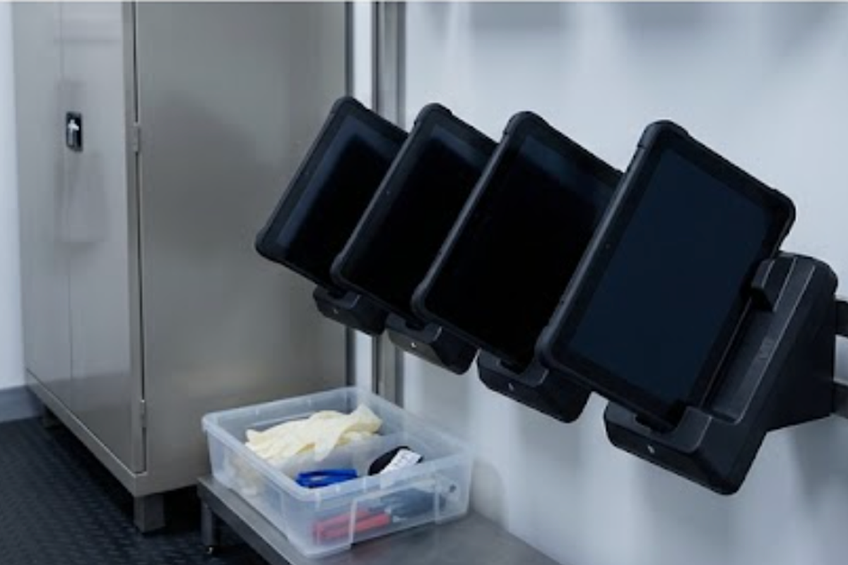 Four rugged tablets charging in wall-mounted cradles in a hospital biomedical equipment room Four rugged tablets charging in wall-mounted cradles in a hospital biomedical equipment room